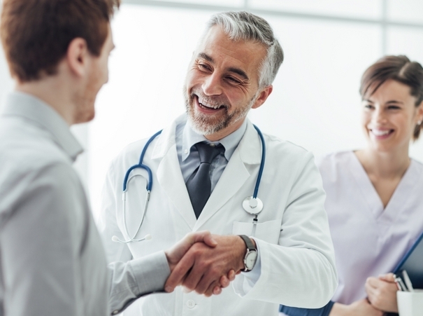 Smiling doctor at the clinic giving an handshake to his patient, healthcare and professionalism concept